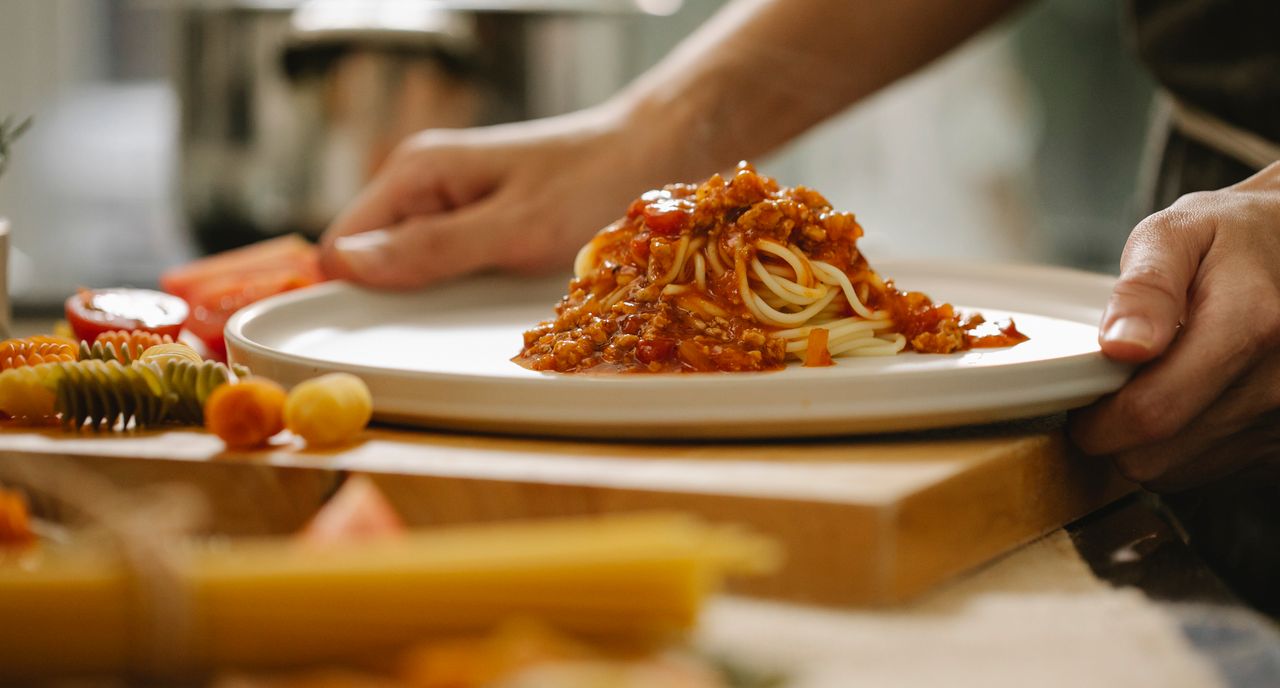 Crop anonymous chef taking portion of delicious pasta with sauce while cooking lunch in kitchen